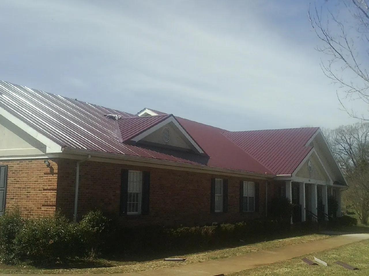 Red metal roof with gabled entries on a long brick building, from a Hail Damage Roof Repair job in Arlington